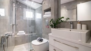 A modern bathroom with a glass-enclosed shower, a toilet, a sink with a mirror, and a plant. - Seaview Modern Loft - Seaview Modern Loft (Zakynthos)