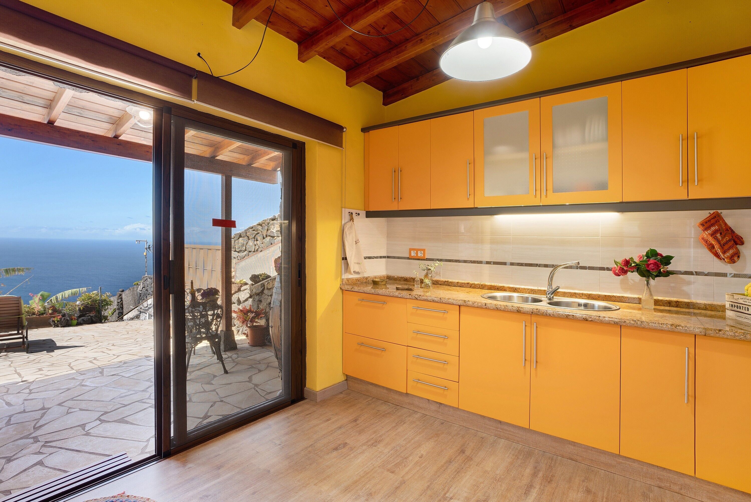 A kitchen with yellow cabinets, a stainless steel sink, and a view through the glass door.