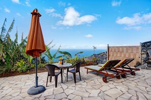 Un patio con tavolo, sedie, ombrellone e poltrone relax vista sull'oceano.