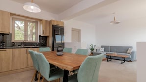A modern kitchen with a wooden table and chairs, a built-in oven, and a grey sofa in the living area. - Spartia Suites - Brand New Seaview Suites - Spartia Suites - Brand New Seaview Suites (Zakynthos)