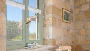 A stone-walled room with a wooden ceiling, a window with a view, a table set with plates, glasses, and a bowl.