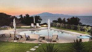 A poolside area with lounge chairs and umbrellas, overlooking a body of water and mountains at sunset. - Niki s Villa - Luxury Seaview Villa - Niki s Villa - Luxury Seaview Villa (Zakynthos)