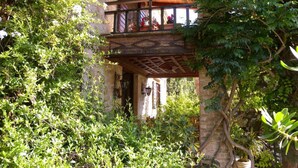 Un balcone in legno con ringhiera in ferro battuto, immerso nel verde e adiacente a un muro in pietra.