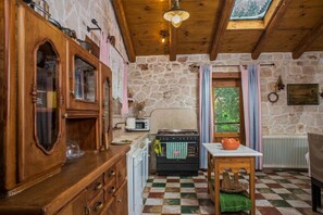 Traditional kitchen with a stone wall, wooden cabinetry, and a gas stove, offering a view of the surrounding greenery.