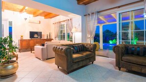 A spacious living room with a large window, a fireplace, and a television. - Zante Sun I - Getaway Villa - Zante Sun I - Getaway Villa (Zakynthos)