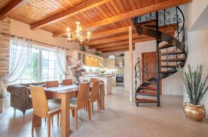 A spacious dining area with a wooden table and chairs, a chandelier, and a view of the kitchen and living area.