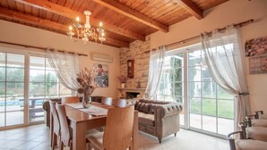 A dining area with a wooden table and chairs, a chandelier, and a stone wall. - Zante Sun I - Getaway Villa - Zante Sun I - Getaway Villa (Zakynthos)