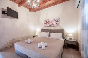 A bedroom with a large bed, two bedside tables, a flat-screen TV mounted on the wall, a chandelier, and a floral artwork above the bed.