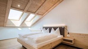 A bedroom with a sloped ceiling, skylights, a bed with pillows, a bedside table, and a wall-mounted lamp.