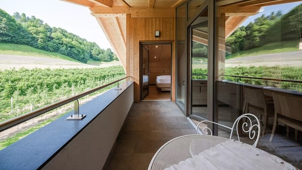 A balcony with a view of a vineyard, wooden ceiling beams, and a bed in the background.