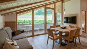 A modern interior with a wooden ceiling, a dining area with a table and chairs, a sofa, and a TV mounted on the wall.