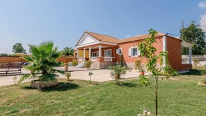 A two-story house with a tiled roof, a front porch, and a small garden with palm trees and shrubs.