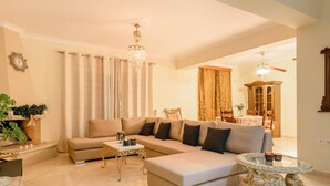 A living room with a beige sectional sofa, a glass coffee table, and a chandelier.