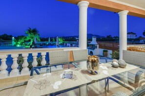 A balcony with a glass table, white balustrades, and a view of a pool area at dusk. - Zante Sun II - Getaway Villa - Zante Sun II - Getaway Villa (Zakynthos)