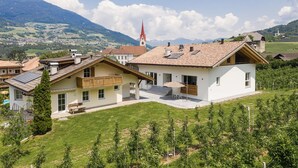 Ein modernes Haus mit einer großen Terrasse, Solaranlage und Blick auf einen Kirchturm.