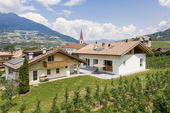 Une maison moderne dotée d’un grand patio, de panneaux solaires et offrant une vue sur le clocher d’une église.