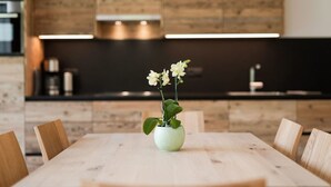 Ein Esstisch mit Stühlen, eine Vase mit Blumen und eine moderne Küche im Hintergrund.