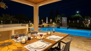 Ein Essbereich im Freien mit Pool, Holzboden und Abendbeleuchtung.