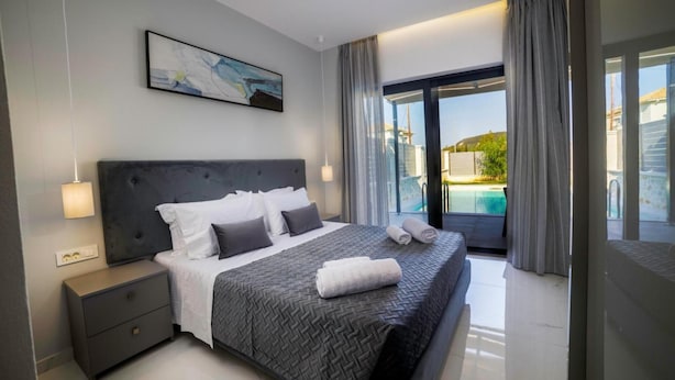 A modern bedroom with a large bed, a nightstand, a painting, and a view of a swimming pool.