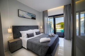 A modern bedroom with a large bed, a nightstand, a painting, and a view of a swimming pool. - Lea Villa - Brand New Modern Villa - Lea Villa - Brand New Modern Villa (Zakynthos)