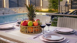 A poolside dining setup with a fruit basket, wine glasses, and plates on a table.