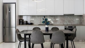 A modern kitchen with white cabinets, a stainless steel refrigerator, a coffee maker, and a vase with flowers on the countertop.
