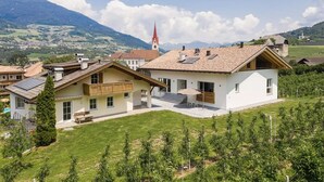 Un immeuble résidentiel doté d’un balcon, d’un petit jardin et offrant une vue sur une montagne et une église en arrière-plan.