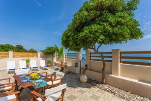 An outdoor dining area with a table set for two, surrounded by chairs, a tree, and a view of the sea. - Villa Elizabeth - Seafront Modern Villa - Villa Elizabeth - Seafront Classic Villa (Zakynthos)