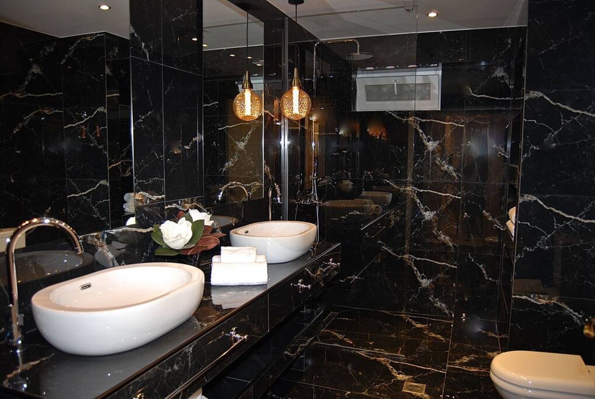 A modern bathroom with two round sinks, a large mirror, and a toilet.