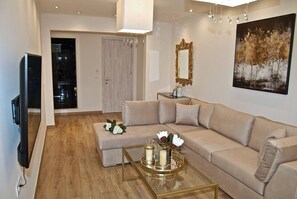 A modern living room with a beige sofa, a glass coffee table with candles, a TV, and a painting on the wall.