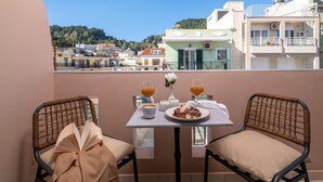 Un balcone con sedie in vimini, un tavolo con un piatto di cibo, due bicchieri di succo d'arancia e un libro.