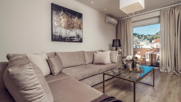Un soggiorno moderno con un divano beige, un tavolino in vetro e una grande finestra vista edifici e colline.