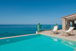 A clear blue pool with two lounge chairs and a stone structure with a tiled roof overlooking the sea. - Villa Bala - Seaside Luxury Villa - Villa Bala - Seaside Luxury Villa (Zakynthos)