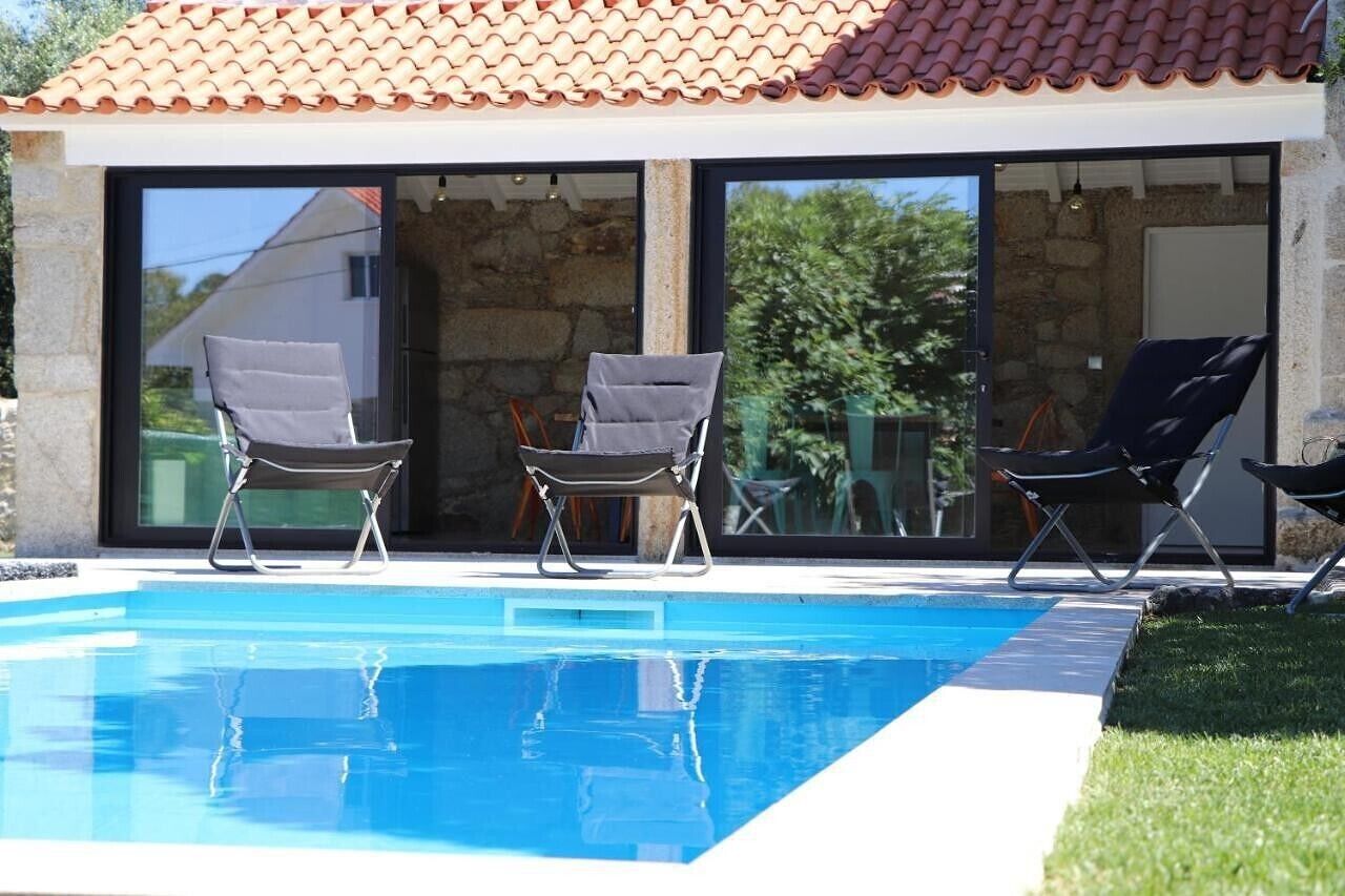 Una piscina con sillas de descanso, fachada de piedra y tejado de baldosas.