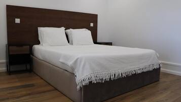 Una habitación de hotel estándar con cabecera de madera, cama con ropa blanca, mesita de noche y suelo de madera.
