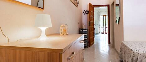 A bedroom with a bed, a bedside table with a lamp, a dresser, and a door leading to another room.