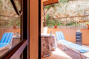 A balcony with two striped lounge chairs, a small table with a decorative item, and potted plants. - Apartment Bilocale Grecale Family Room (Viticcio)