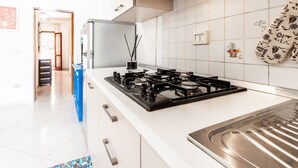 Una cuina moderna amb fogó a gas, armaris blancs i nevera blava.