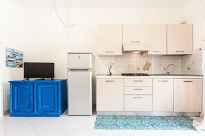 Una cocina con armarios blancos, un mueble azul, un refrigerador blanco y una alfombra estampada.