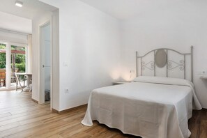 A bedroom with a bed, a nightstand, a window, and a door leading to a balcony.