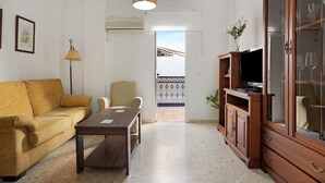 A living room with a sofa, a table, a TV on a cabinet, and a door leading outside. - Holiday Home 'Casa Begines' close to City Centre with Shared Pool (Vejer)