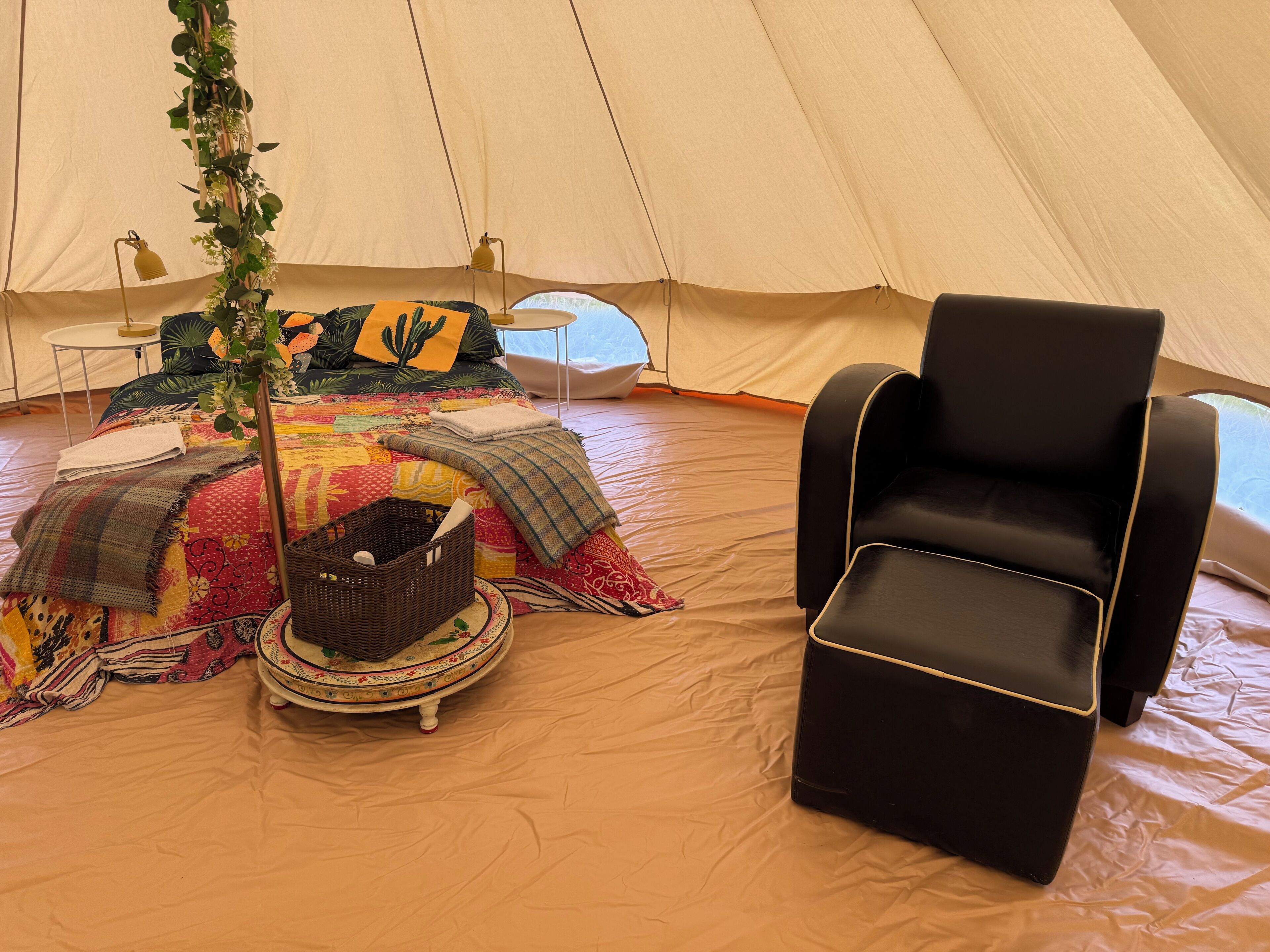 A tent with a bed, a black chair, and a small table with a lamp.