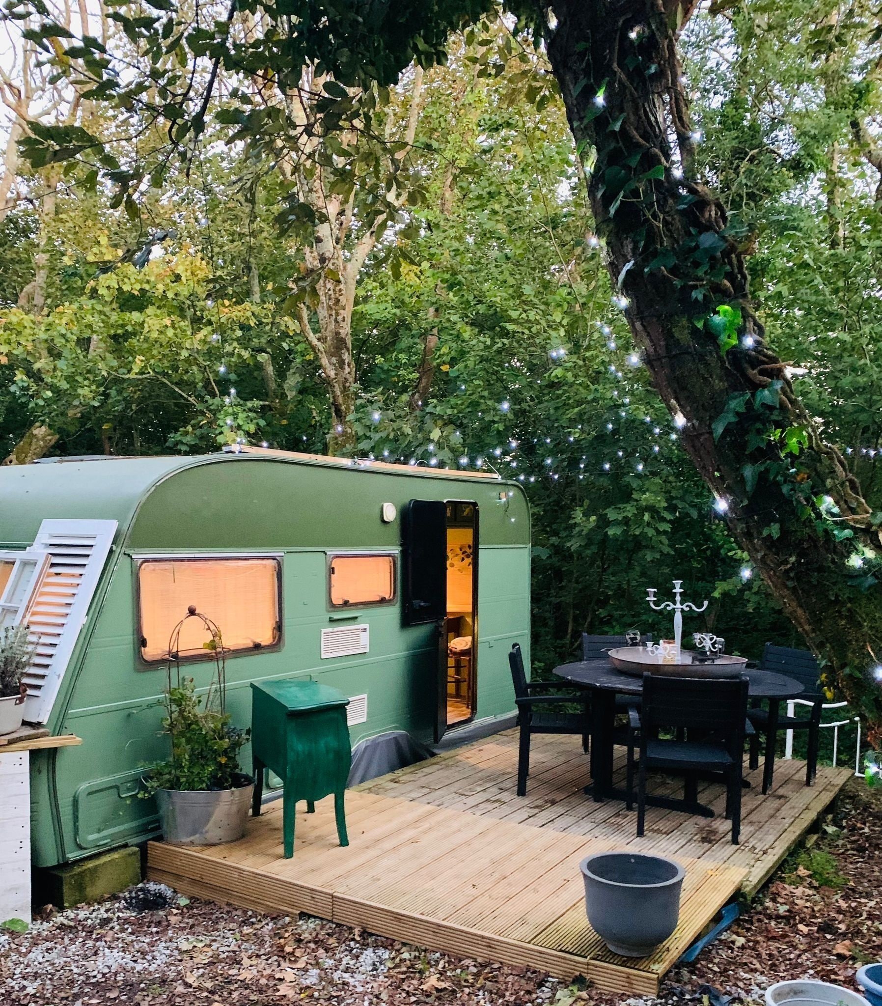 Ein grüner Wohnmobilwagen mit Holzterrasse, Sitzgelegenheiten im Freien und einem Esstisch.