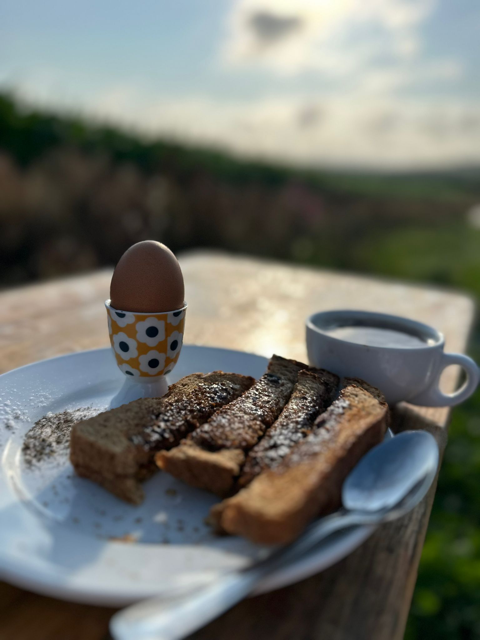 A plate with toast and a boiled egg on a wooden table outdoors.