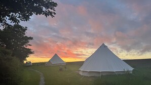 Deux tentes blanches se dressent dans un champ verdoyant, un sentier menant à elles.
