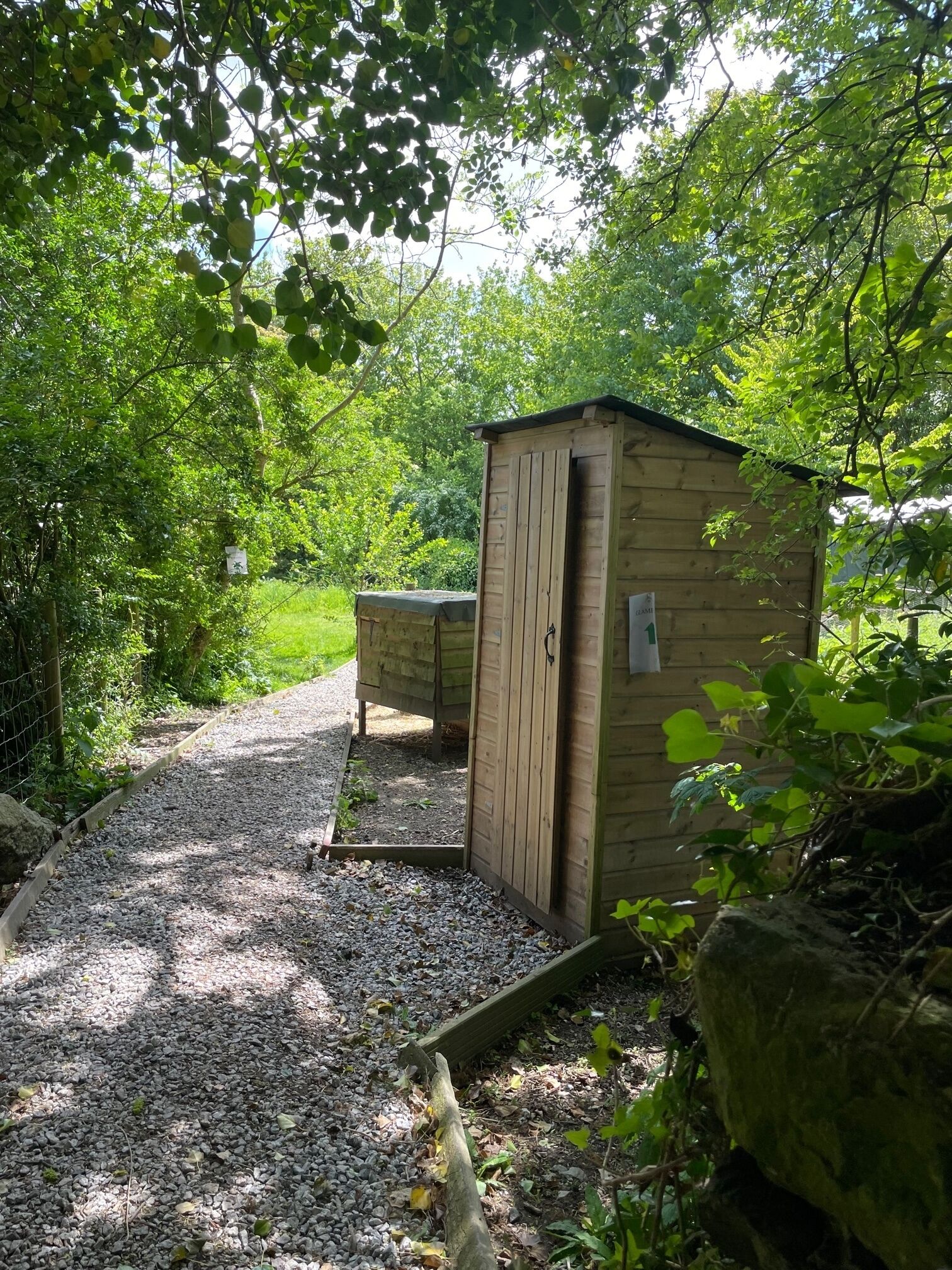 Un abri en bois avec une porte, entouré de gravier et de verdure.