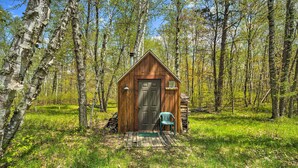 A wooden cabin with a door, a bench, and a lamp post in a forest.
