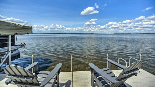 A dock with two chairs facing a calm body of water under a clear sky.