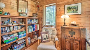 A wooden cabin interior with a bookshelf, a chair, a lamp, and a framed picture on the wall.