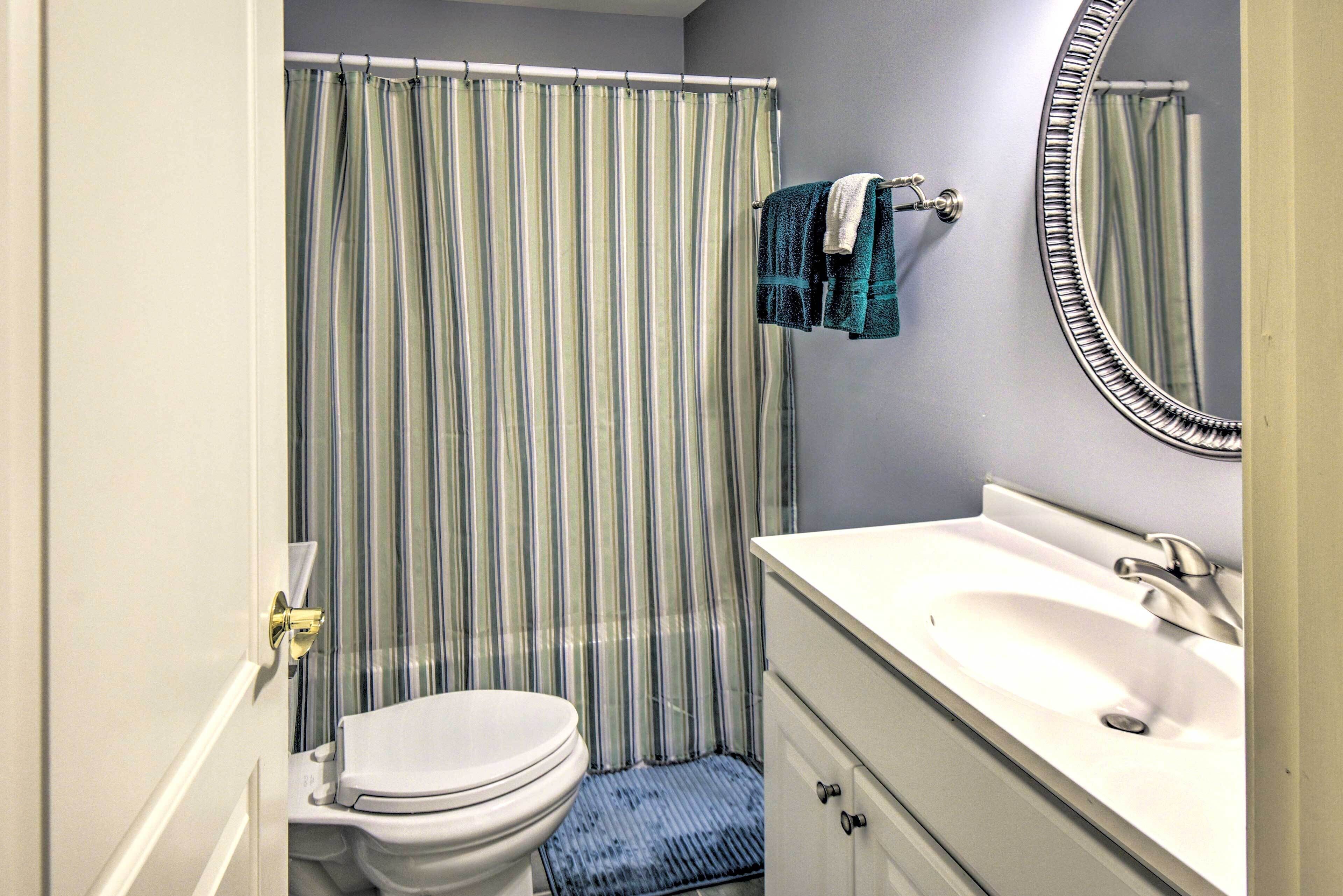 Une salle de bain avec un rideau de douche à rayures, des toilettes blanches, un lavabo avec un miroir et des serviettes suspendues à un porte-serviettes.